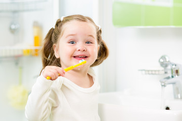 smiling kid girl brushing teeth in bathroom