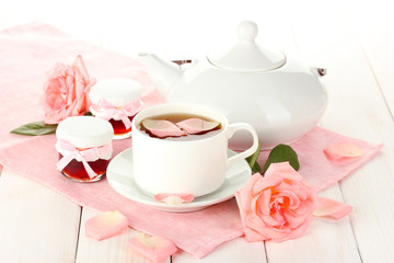 teapot and cup of tea with roses and jam on white wooden table
