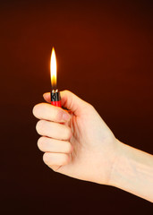 Burning lighter in female hand, on dark brown background