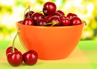 Cherry berries in bowl on table on bright background