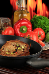 Piece of fried meat on pan on wooden table on fire background