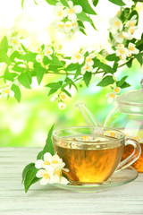 Cup of tea with jasmine, on wooden table, on bright background