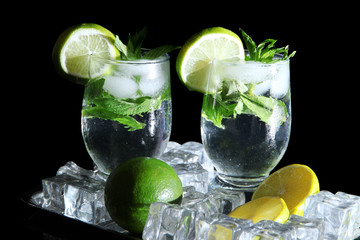 Glasses of cocktail with ice on metal tray on black background