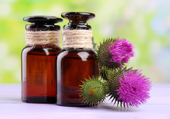Medicine bottles with thistle flowers on nature background