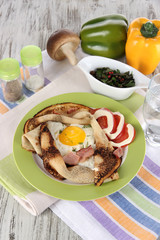 Scrambled eggs and pancake on plate on napkin on wooden table
