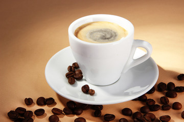 Cup of coffee with coffee beans on beige background