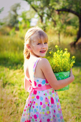 Smiling little girl with a bucket of flowers in the park