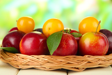 Ripe plums in basket on wooden table on natural background