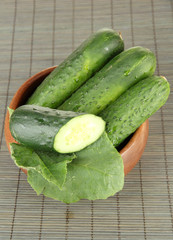 Tasty green cucumbers in wooden bowl, on bamboo mat background