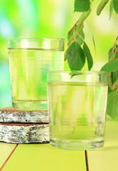 Glasses of birch sap on wooden table, on green background