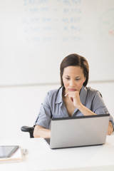 Businesswoman With Hand On Chin Using Laptop In Office