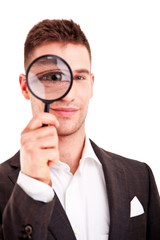 Young business man in suit looking to magnifying glass