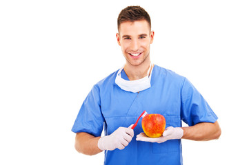 Handsome dentist brushing apple with toothbrush, isolated on