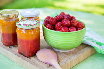 Homemade strawberry jam in different jars and fresh ripe strawbe