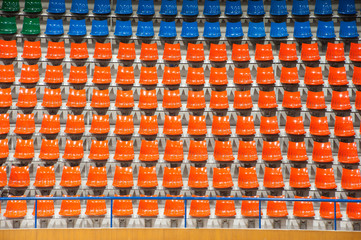 Plenty of orange and blue plastic seats at stadium .