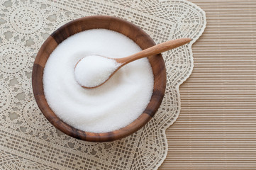 Bowl of white sugar with wooden spoon.