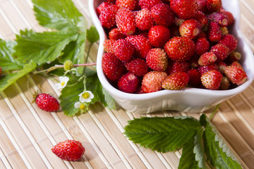 Wild strawberries in a small bowl, surrounded by leaves