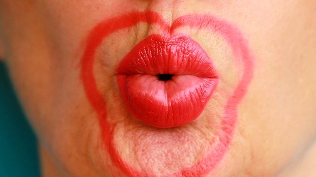 Il bacio / Una bocca rossa con rossetto soffia un bacio a forma di cuore con amore, passione e seduzione