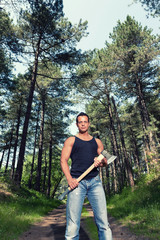 Muscled man with black shirt and axe in forest.