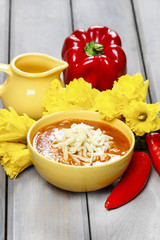 Bowl of tomato soup, fresh flowers and vegetables in the backgro