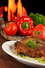 Piece of fried meat on plate on wooden table on fire background