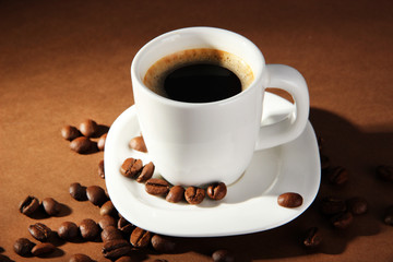 Cup of coffee with coffee beans on brown background