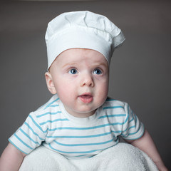 Portrait of a little boy in a chef hat on a gray background