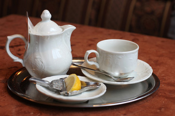 Fototapeta premium Teapot with cup and bit of lemon on table in cafe