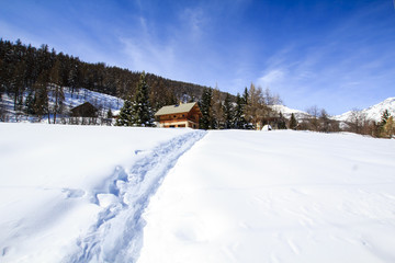 Way made in snow towards wooden chalet in Alps