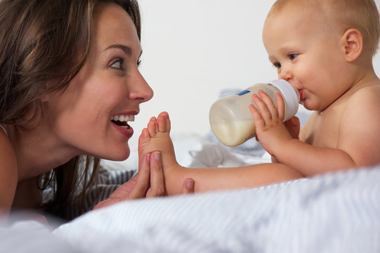 Baby drinking from bottle with mother smiling