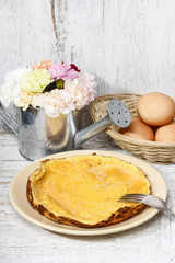 Omelette on white wooden table, eggs in the background