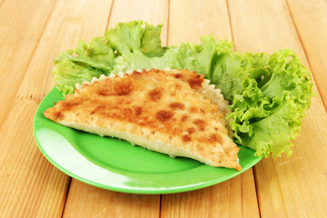 Tasty chebureks with fresh herbs on plate,on wooden background