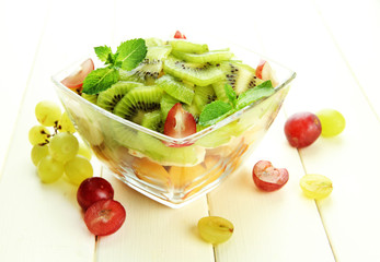 Tasty fruit salad in glass bowl, on white wooden table