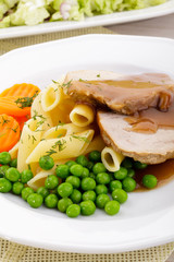 Roasted pork shoulder served with pasta and vegetables
