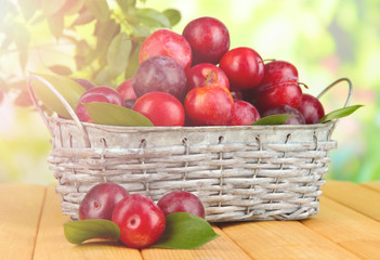 Ripe plums in basket on wooden table on natural background