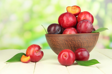 Ripe plums in bowl on wooden table on natural background