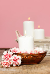 Obraz na płótnie Canvas White candle among carnation flowers in vintage wooden bowl