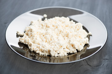 Glass plate with fresh cottage cheese on black wooden boards