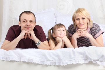 Obraz na płótnie Canvas Happy father, little daughter and mother lie on white double bed