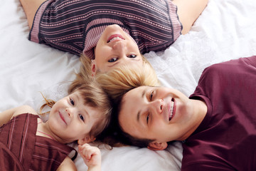 Happy father, little daughter and mother lie on white double bed