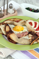 Scrambled eggs and pancake on plate on napkin on wooden table