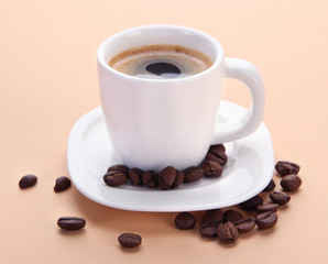 Cup of coffee with coffee beans on beige background