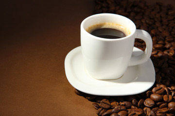 Cup of coffee with coffee beans on brown background