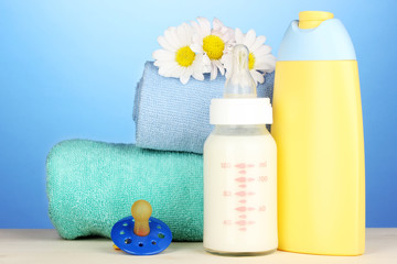 Obraz na płótnie Canvas Dziecko butelki mleka i szampon w pobliżu ręczniki na niebieskim tle