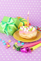 Colorful birthday cake with candle and gifts on pink background