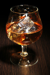 Brandy glass with ice on wooden background