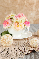 Roses in cup on napkins on  wooden table on beige background
