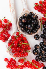 Red and black currant in wooden spoons isolated on white