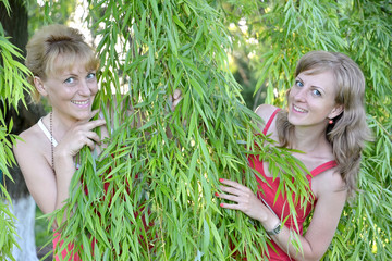 Two young women look because of willow branches