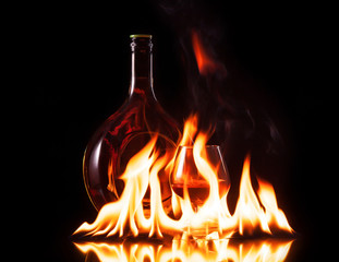 Bottle glass of cognac in fire flame on black background
